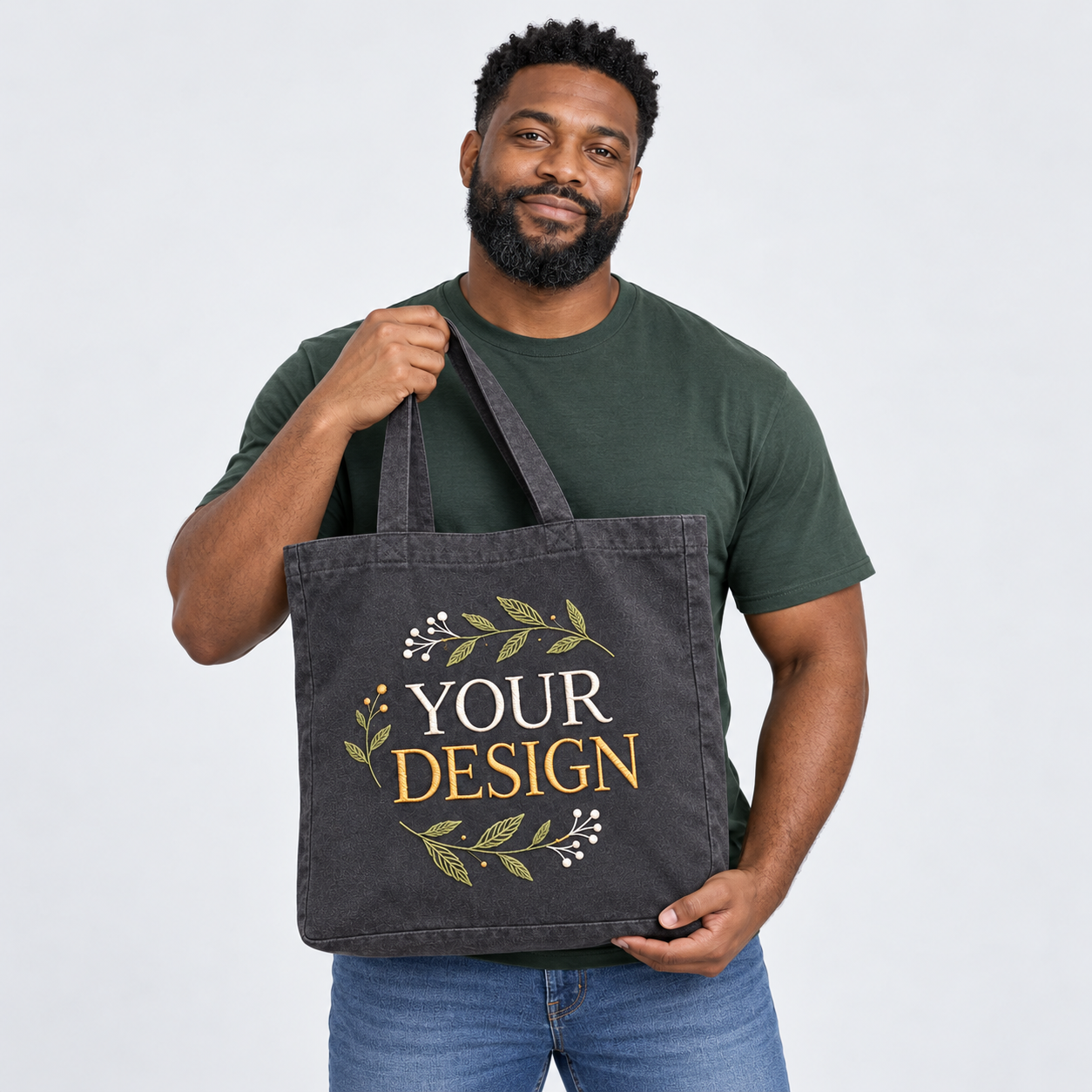 Man holding a charcoal tote embroidered with YOUR DESIGN and leaves against a light studio backdrop
