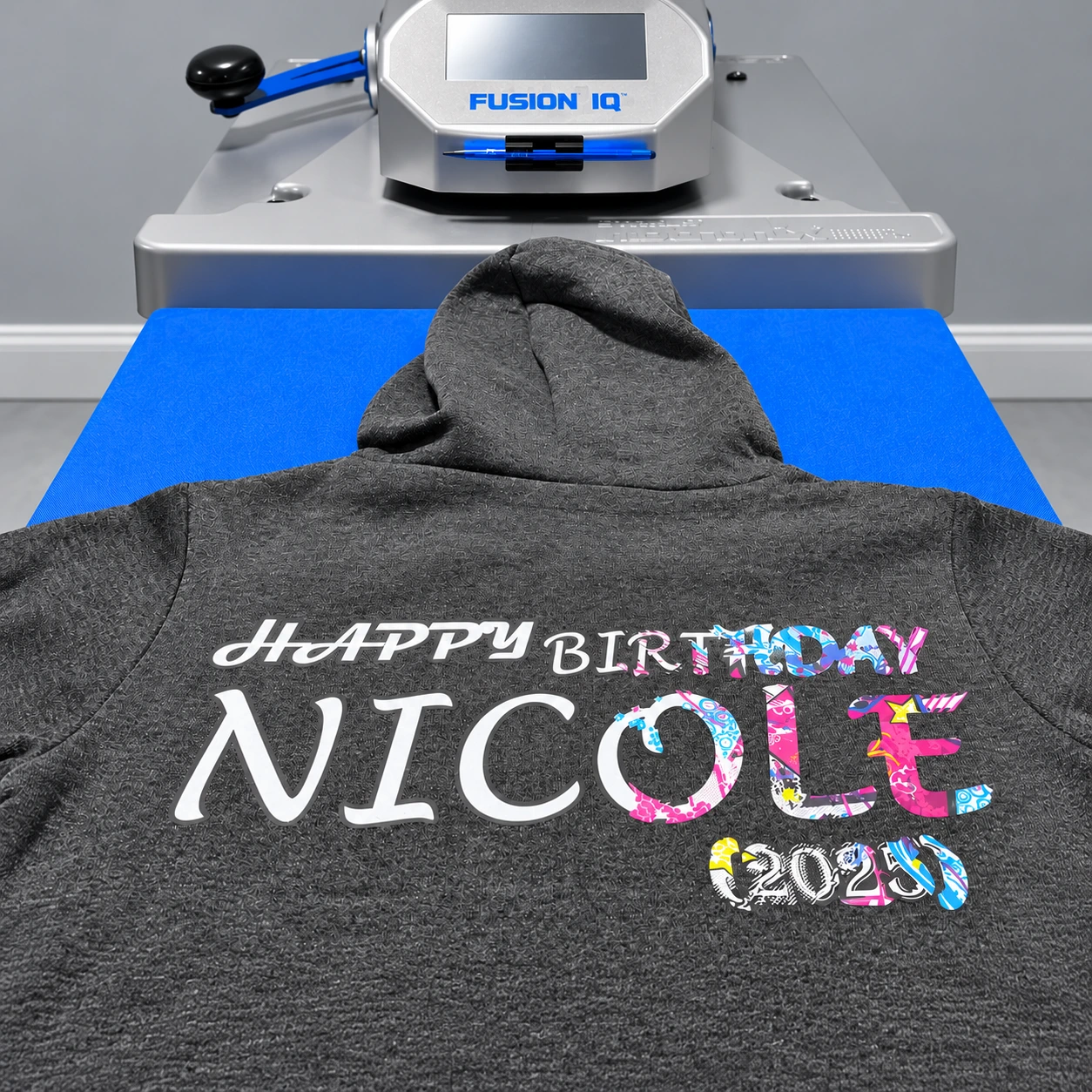 Gray hoodie with a colorful birthday print beneath a heat press